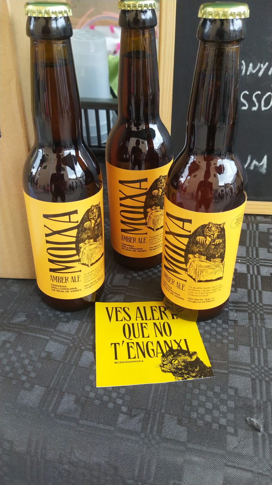 Tres botelles de cervesa moixa i una ferratina on es veu la imatge de marca